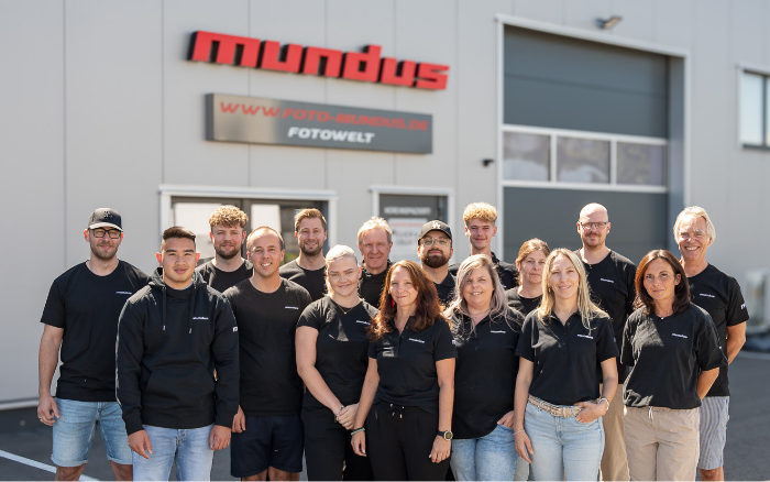 Das Team von Foto Mundus steht lächelnd vor dem Firmengebäude und präsentiert stolz das neue Shopdesign